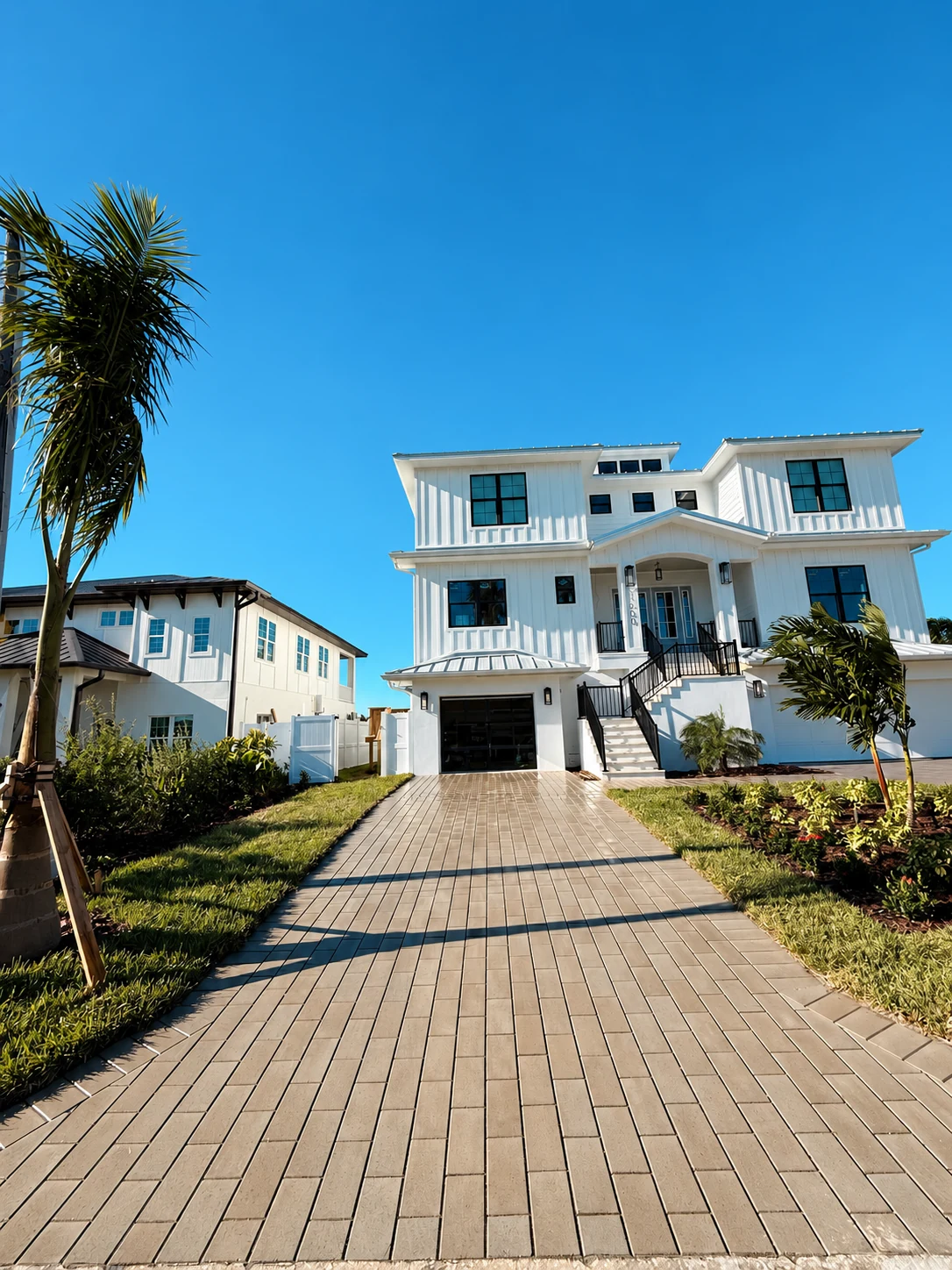 Warm neutral paver driveway extends from the street to the garage between landscaped borders.